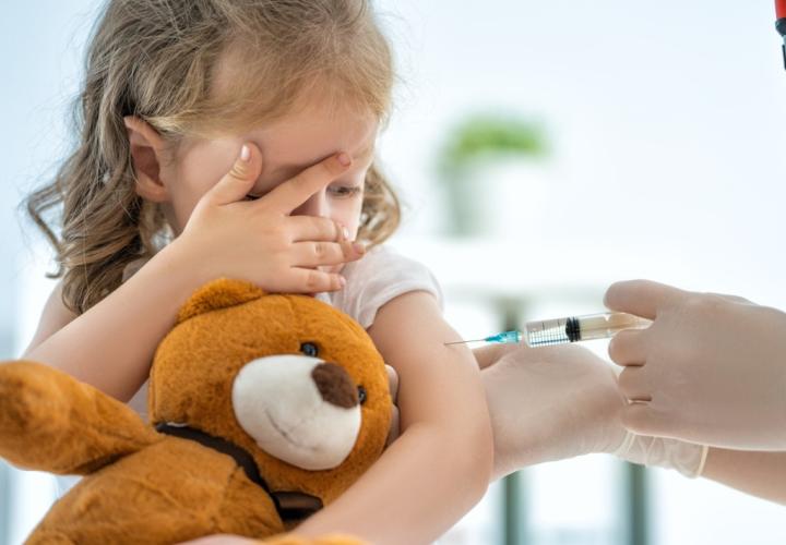 Young girl, scared, getting vaccine and holding teddy bear