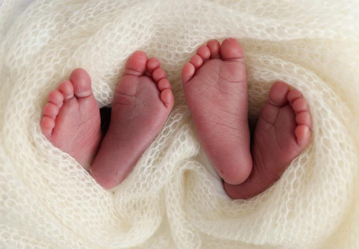 Two pairs of newborn twin feet sticking out from white blanket