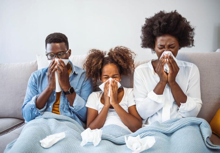 Family of 3, sneezing into tissues on couch.