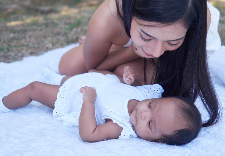 Mom and infant baby outside on blanket, wearing white.