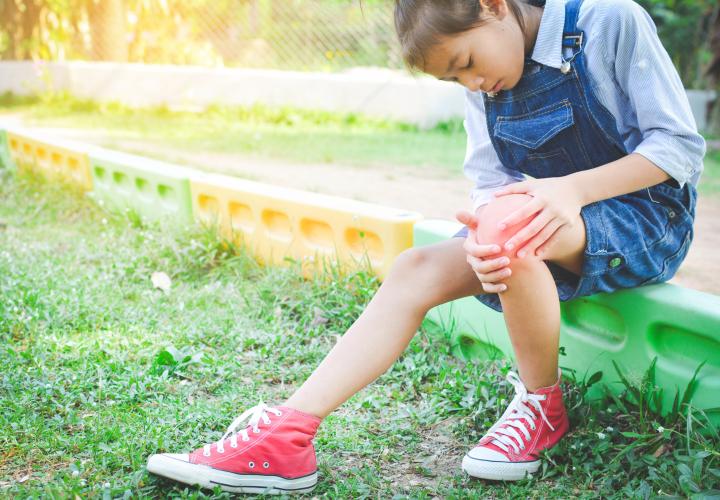 Young girl outside grabbing knee, joint pain and arthritis in kids