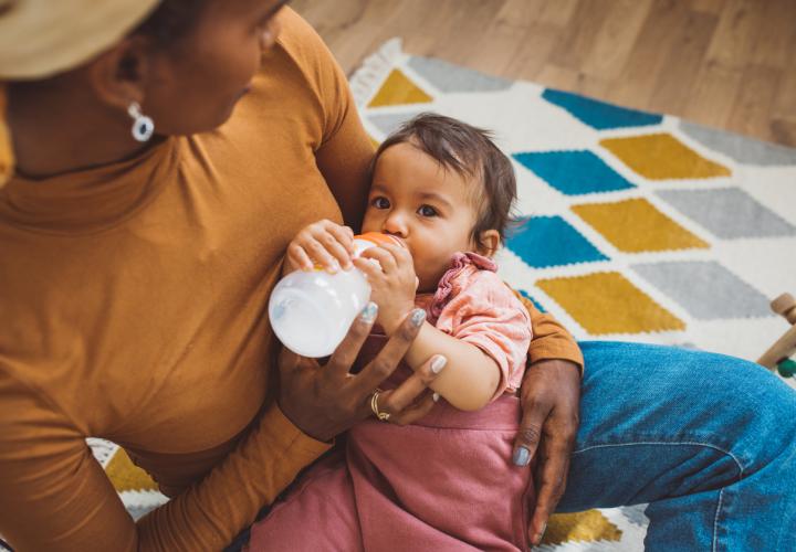 Baby drinking bottle in mother's arms.