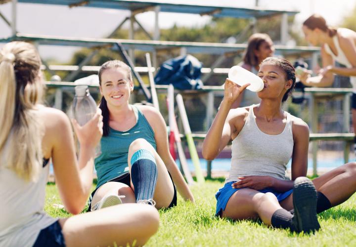 Group of teen female athletes drinking water on field