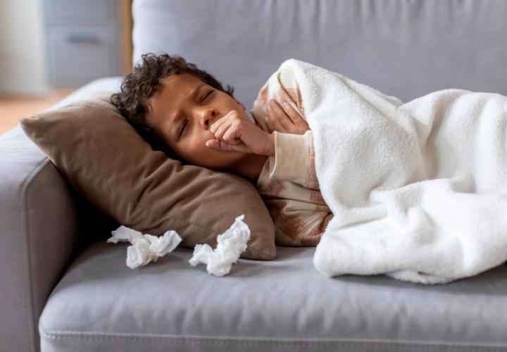 Sick school-aged boy on couch, coughing with tissues