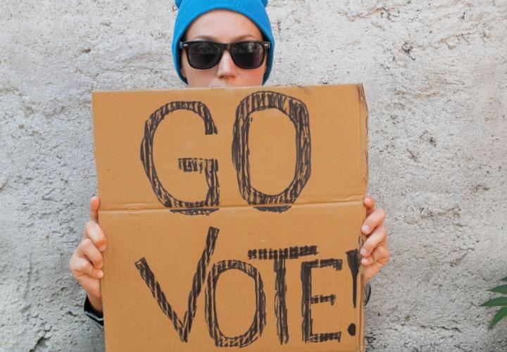 Young woman holding up cardboard sign that says Go Vote!