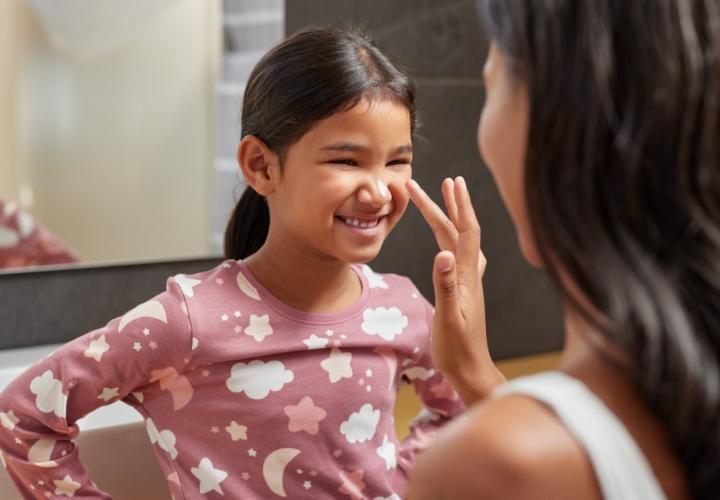 Mom applying lotion on young girl's face. Safe skincare for kids and teens