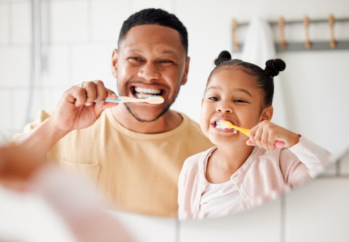 Father and daughter brushing teeth together.