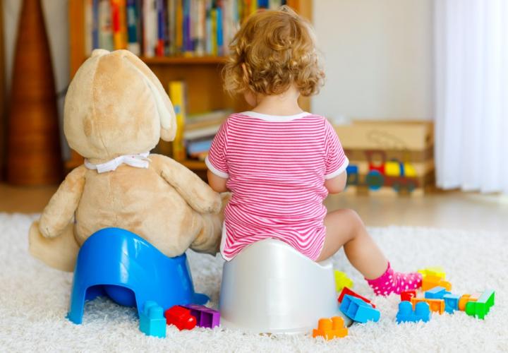 Cute toddler girl sitting on potty next to stuffy on its potty. Backs only