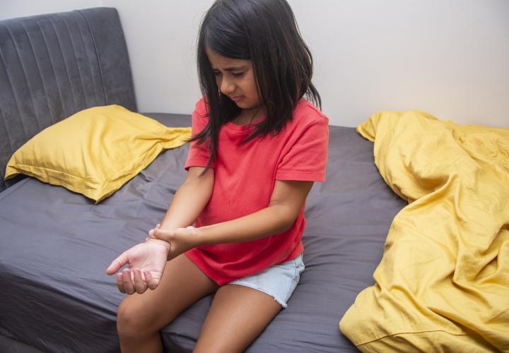 Little girl, maybe with carpal tunnel syndrome, sitting on bed grabbing wrist in pain