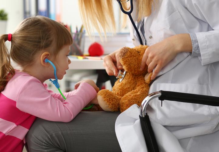 Young girl listening to teddy bear's heart on doctor's lap