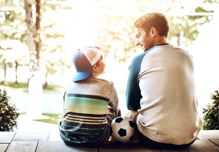 Father and young son, sitting on steps, soccer ball in between them. 