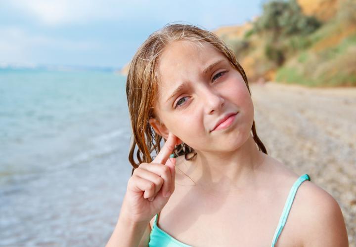 The child got water in his ear while swimming in the sea. The girl cleans her ear from water