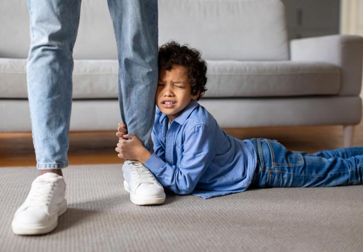 Young boy having tantrum, clinging to parent's leg, laying on floor