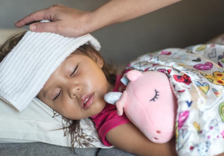 Young girl, sick in bed holding pink unicorn stuffed animal, with cloth over her head