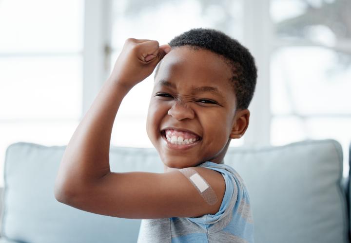 Young boy, flexing bicep with bandaid, proud after getting vaccine