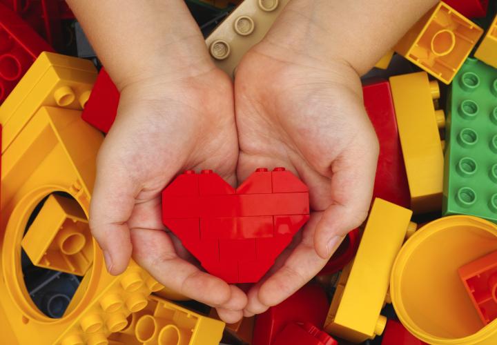 Small child hands holding heart-shaped lego blocks