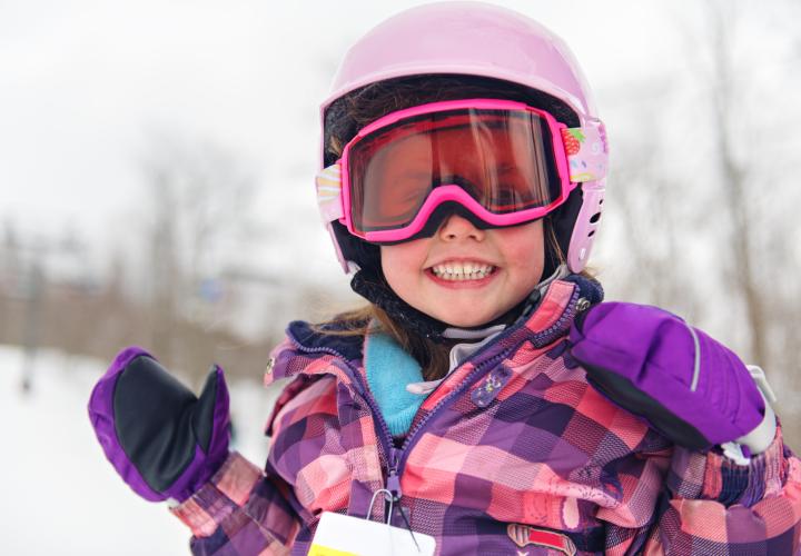 A child playing in the snow wearing ski goggles and ski helmet. 
