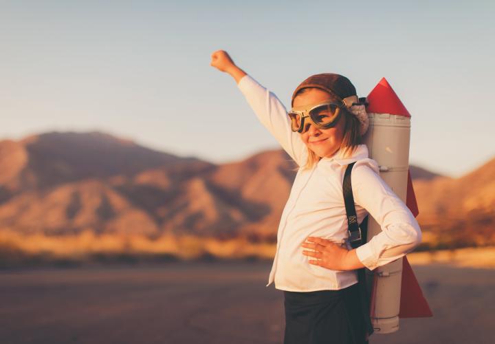 Child with pilot goggles on and a rocket backpack. 