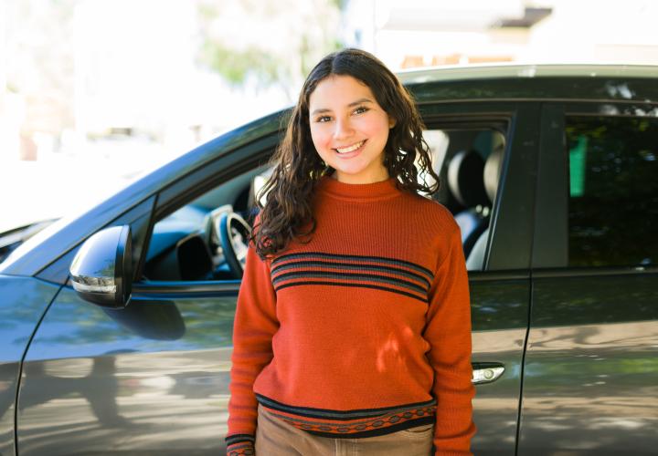 Teen driver standing in front of car