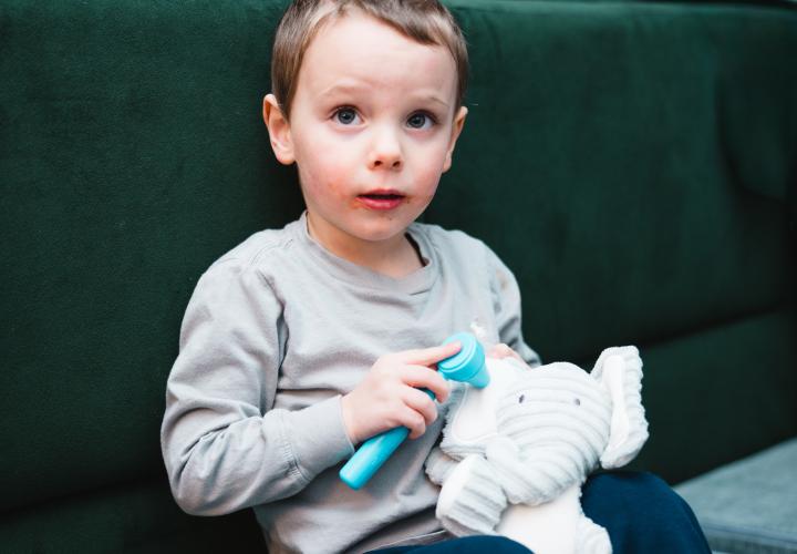 A toddler uses a plastic otoscope to look in a stuffed elephant's ear.