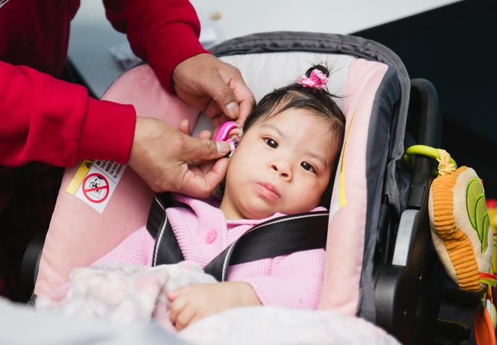 An infant receives a hearing aid adjustment in an audiology visit.