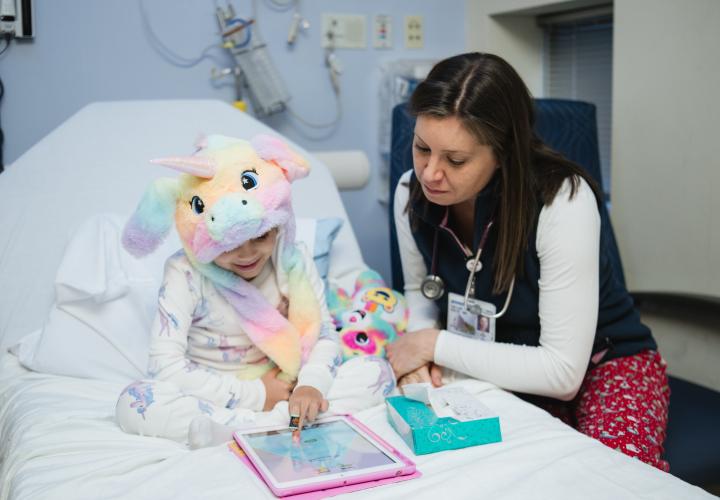 A hem-onc patient seated in a hospital bed shows a doctor her i-pad.