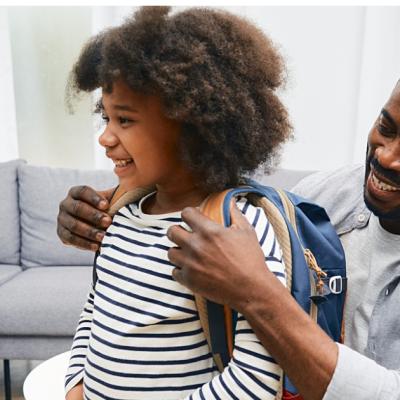 A dad helps his child put their backpack on