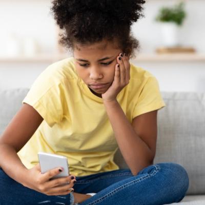 A young girl sits and looks sadly at her phone