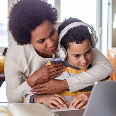 A mother hugs her son while he's on the computer
