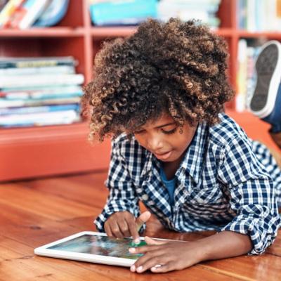 Young boy lies on the ground and plays with a tablet