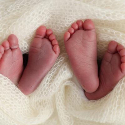 Two pairs of newborn twin feet sticking out from white blanket