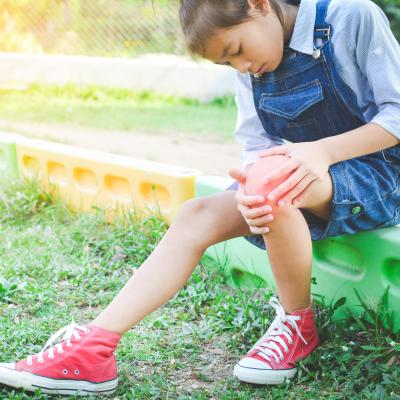 Young girl outside grabbing knee, joint pain and arthritis in kids