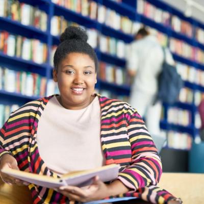 Teenage or young adult woman sitting in library, smiling