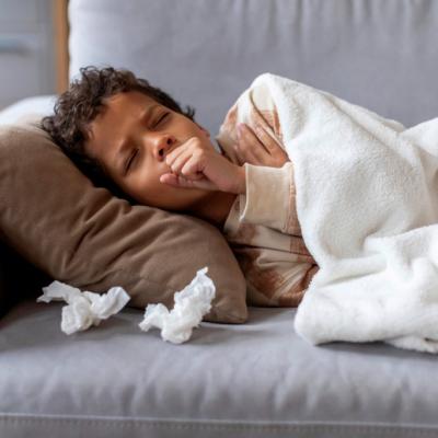 Sick school-aged boy on couch, coughing with tissues