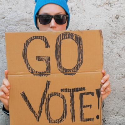 Young woman holding up cardboard sign that says Go Vote!
