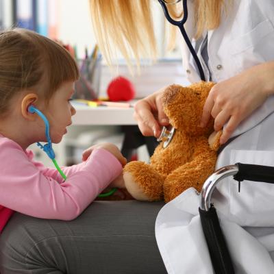 Young girl listening to teddy bear's heart on doctor's lap