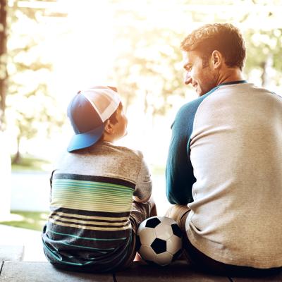 Father and young son, sitting on steps, soccer ball in between them. 