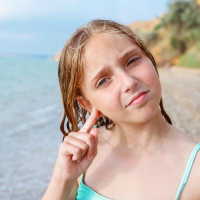 The child got water in his ear while swimming in the sea. The girl cleans her ear from water