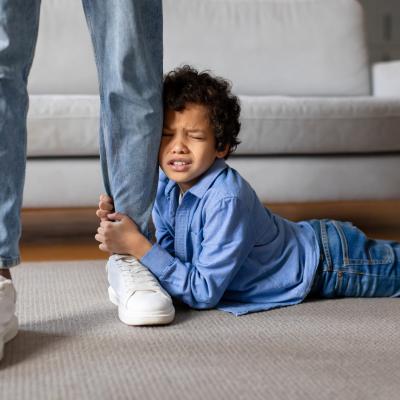Young boy having tantrum, clinging to parent's leg, laying on floor