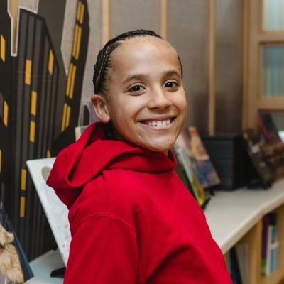 School-aged boy smiling in library, wearing red sweatshirt