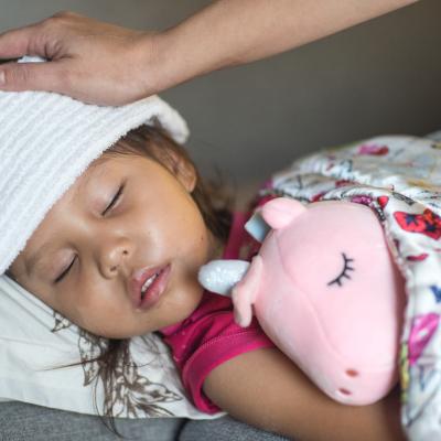 Young girl, sick in bed holding pink unicorn stuffed animal, with cloth over her head