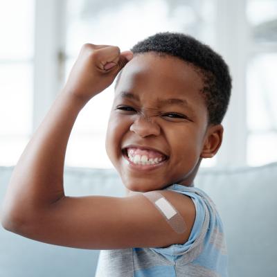 Young boy, flexing bicep with bandaid, proud after getting vaccine