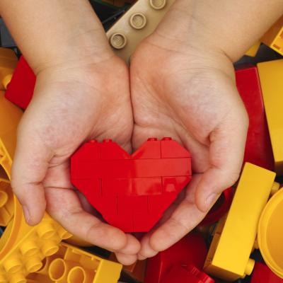 Small child hands holding heart-shaped lego blocks