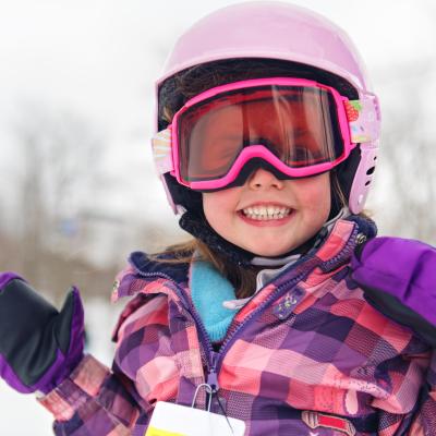 A child playing in the snow wearing ski goggles and ski helmet. 