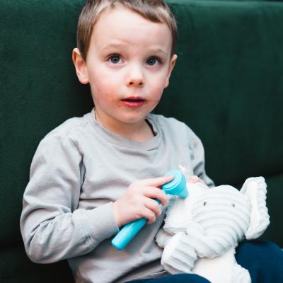 A toddler uses a plastic otoscope to look in a stuffed elephant's ear.
