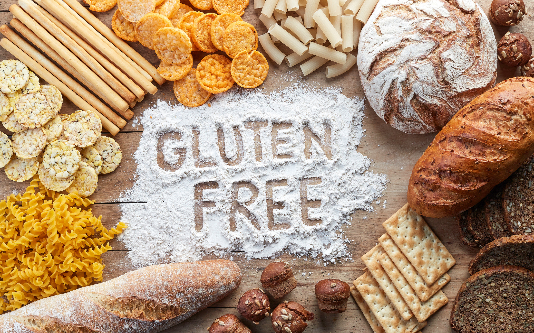 Rice, pastas and breads surrounding a pile of flour in which "gluten free" is written