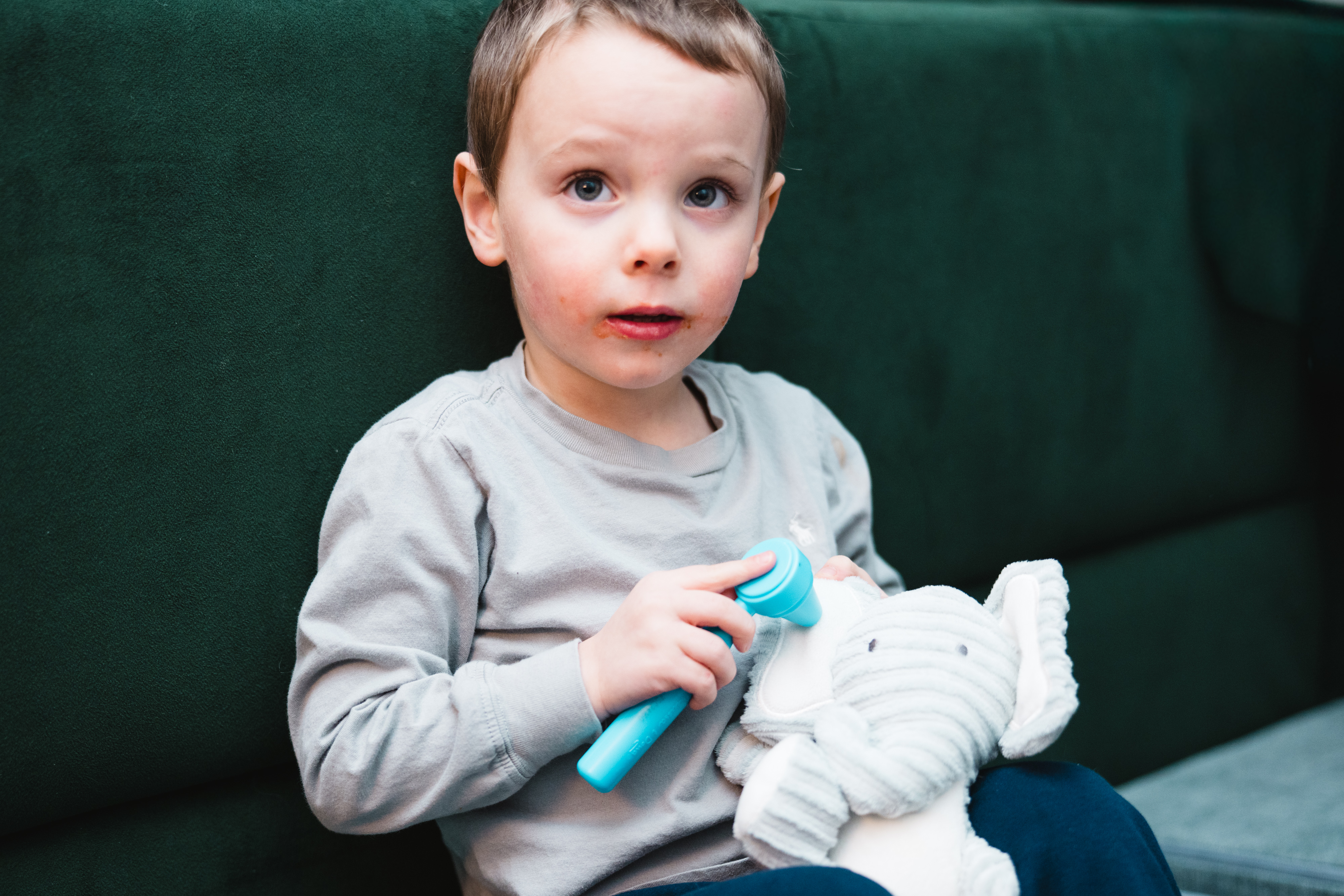 A toddler uses a plastic otoscope to look in a stuffed elephant's ear.