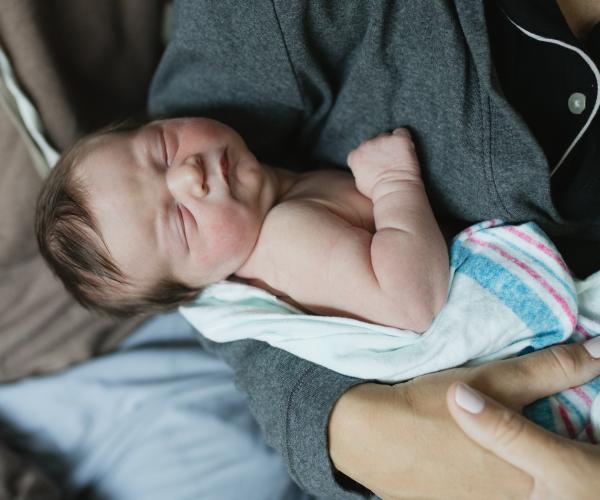 newborn baby sleeping in parent's arms and hospital blanket